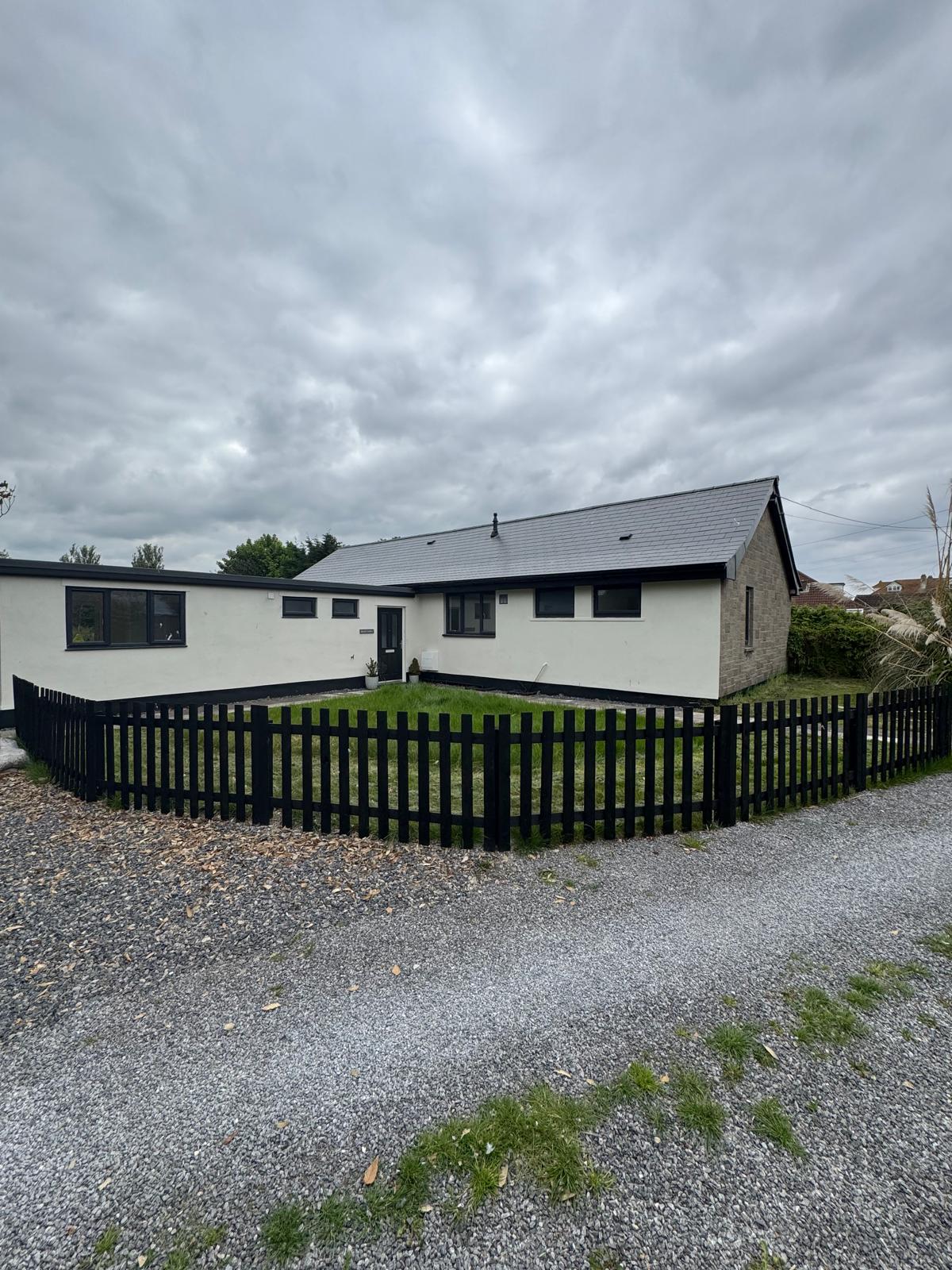 Complete exterior view of white bungalow with dark trim and black fencing